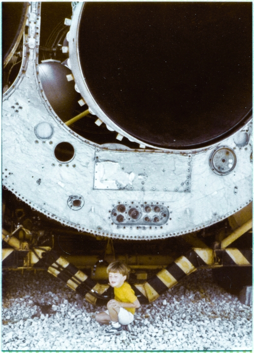 Kai MacLaren pauses to rest for a moment in the shade of the Booster Engine of the Atlas ICBM supported on its transport semitrailer, which was on display at the Air Force Space and Missile Museum at Cape Canaveral Air Force Station, Florida. To the left of the large round dark opening of the Booster Engine nozzle, a bit of one of the spherical tanks which held pressurized gas used to for fuel and oxidizer tank pressurization as well as a variety of other systems which required pressurized gas to function, can be seen, and in the darkness beyond that, a bit of the turbomachinery which powered the engine can also be seen. Photograph by James MacLaren.